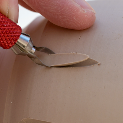 Hand using a small tool to cut into a piece of clay
