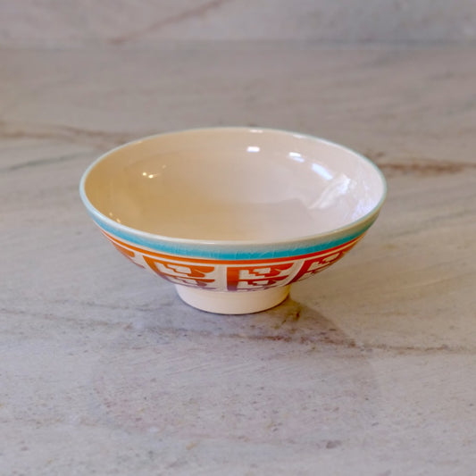 A small ceramic bowl with a cream-colored interior, a turquoise rim stripe, and orange Chinese characters printed on the exterior, set on a light marble surface.