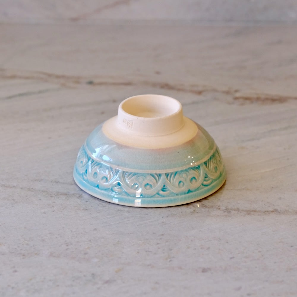 A small ceramic cup or bowl turned upside down on a light marble surface, featuring a light blue and white patterned exterior and a cream-colored interior.