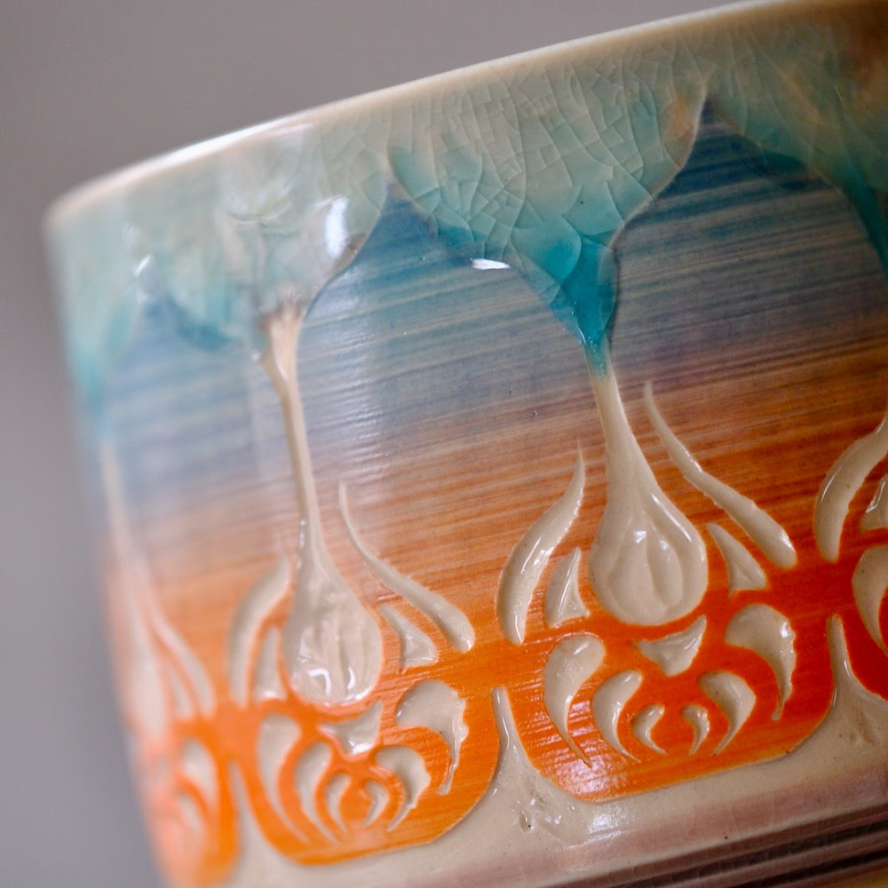 Close-up of a glazed ceramic bowl featuring a textured, dripping design in teal, blue, orange, and cream.