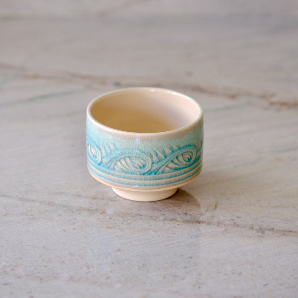 A small ceramic sake cup with a light blue and white wave pattern, set on a light gray marble surface.