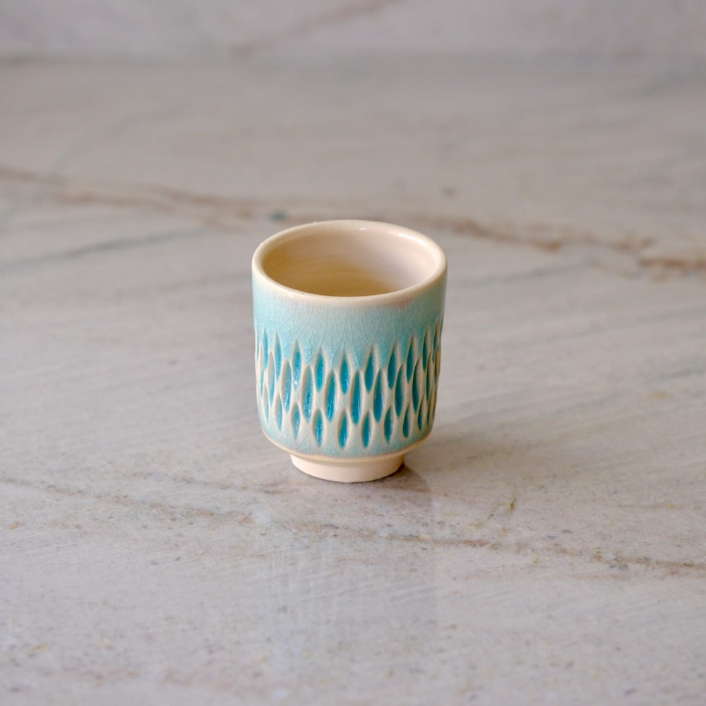 A small ceramic teacup with a light blue and white textured pattern, set on a light gray marble surface.