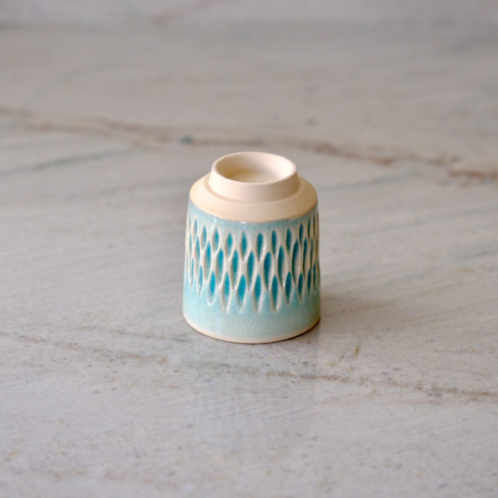 A small ceramic candle holder with a light blue and cream textured pattern, shown on a light gray marble surface.